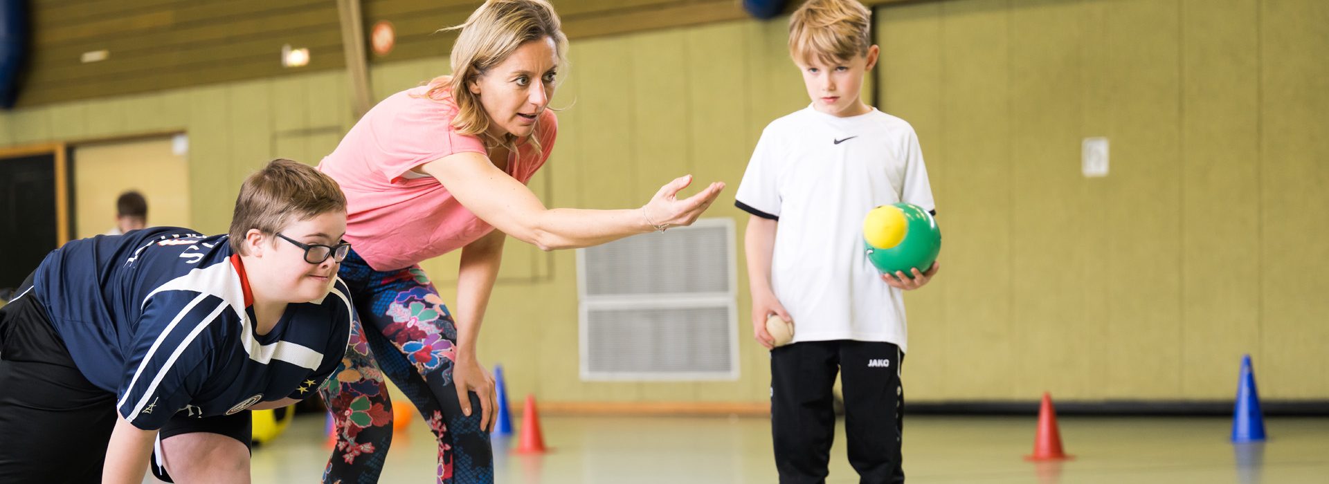 Übungsleiterin mit 2 Jungen in Turnhalle (Inklusion)